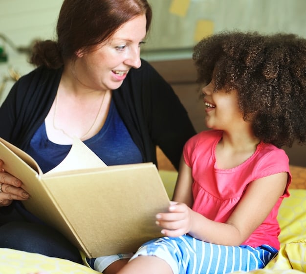 A close-up shot of a social worker reading a colorful storybook to a young child in a comfortable living room setting. The child is engaged and smiling, while the social worker is pointing at the pictures in the book.