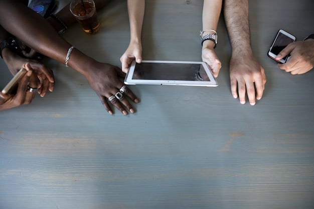 A diverse group of people gathered around a table, collaborating on a social project plan using a digital tablet and various technology devices.
