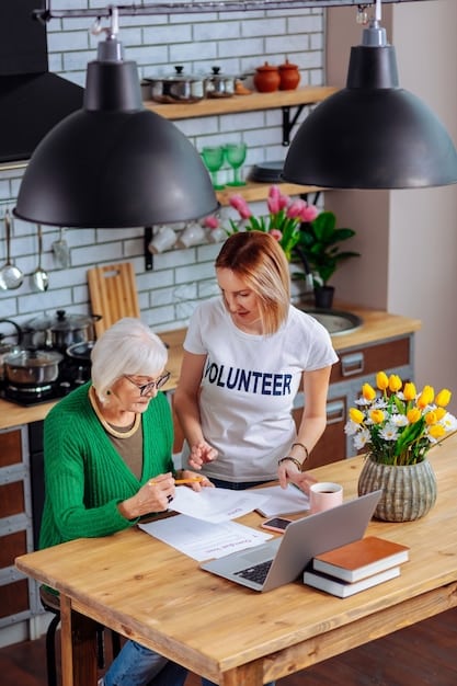 A volunteer is sitting at a table with a woman, reviewing her budget on a spreadsheet. They are both smiling and engaged in the conversation. The background is a brightly lit office with other people working at desks.