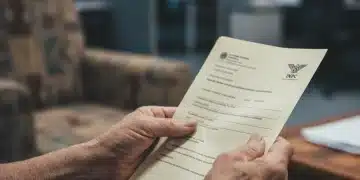Mãos de idoso segurando documento do BPC 2026 em frente a um balcão de atendimento
